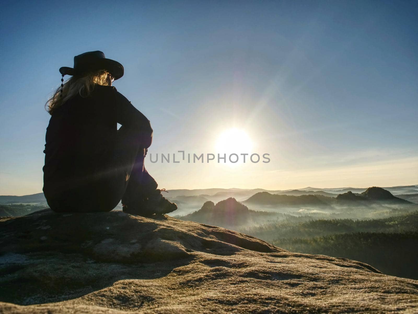 Cute light hair woman enjoying the outdoors at the mountain. Sports figure sit on rough rocky ground