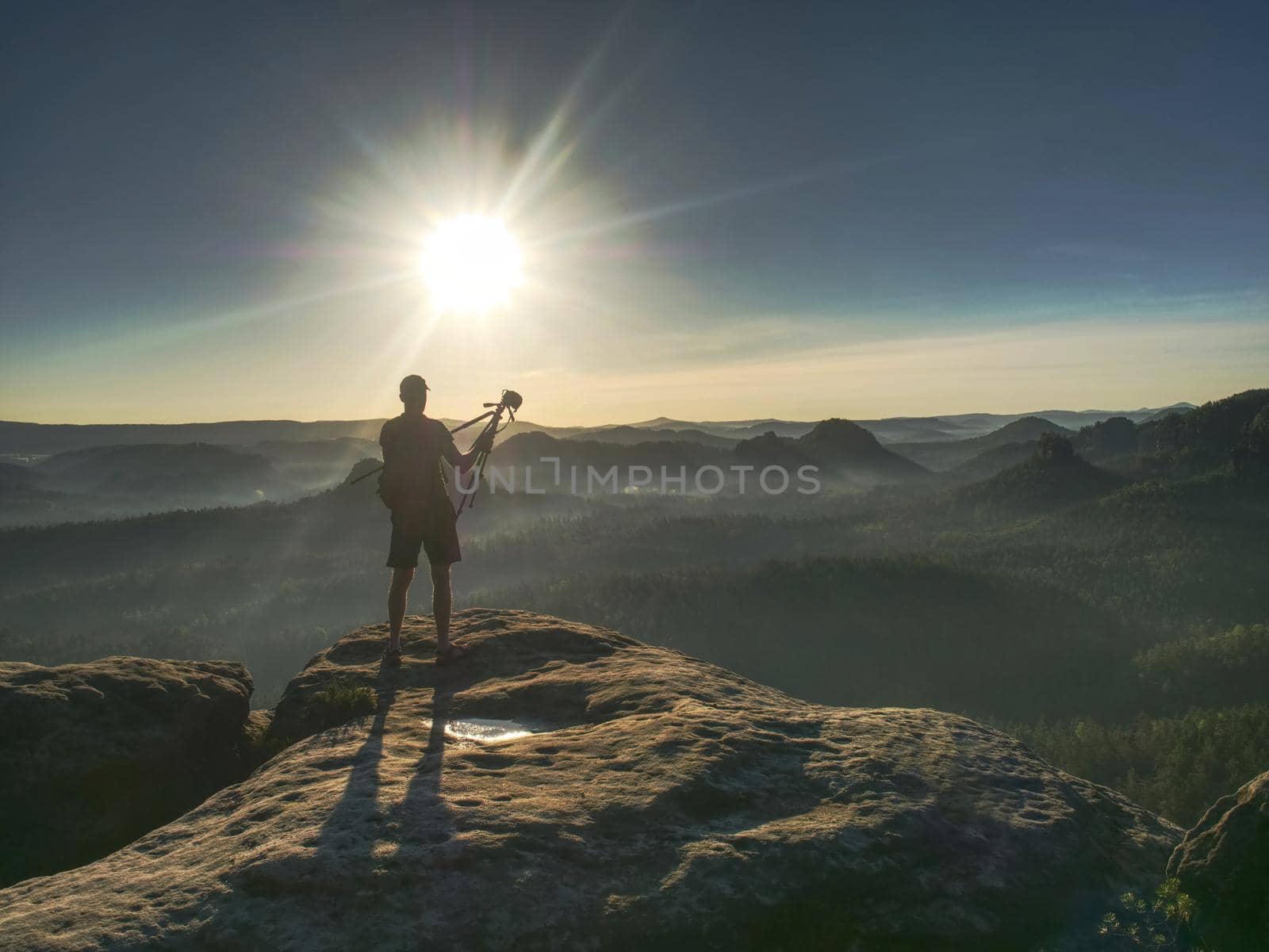Man photographer taking photo on sunset mountain peak. Hiker in shorts and backpack on sweaty bag