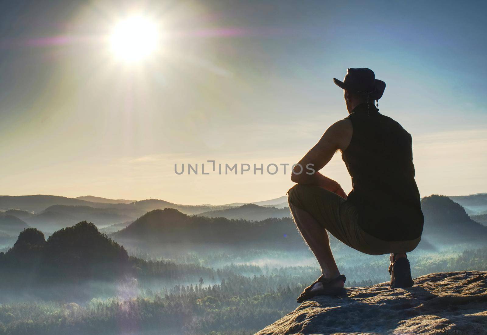 Person rests a top a high peak gazing into the sunset in the distance