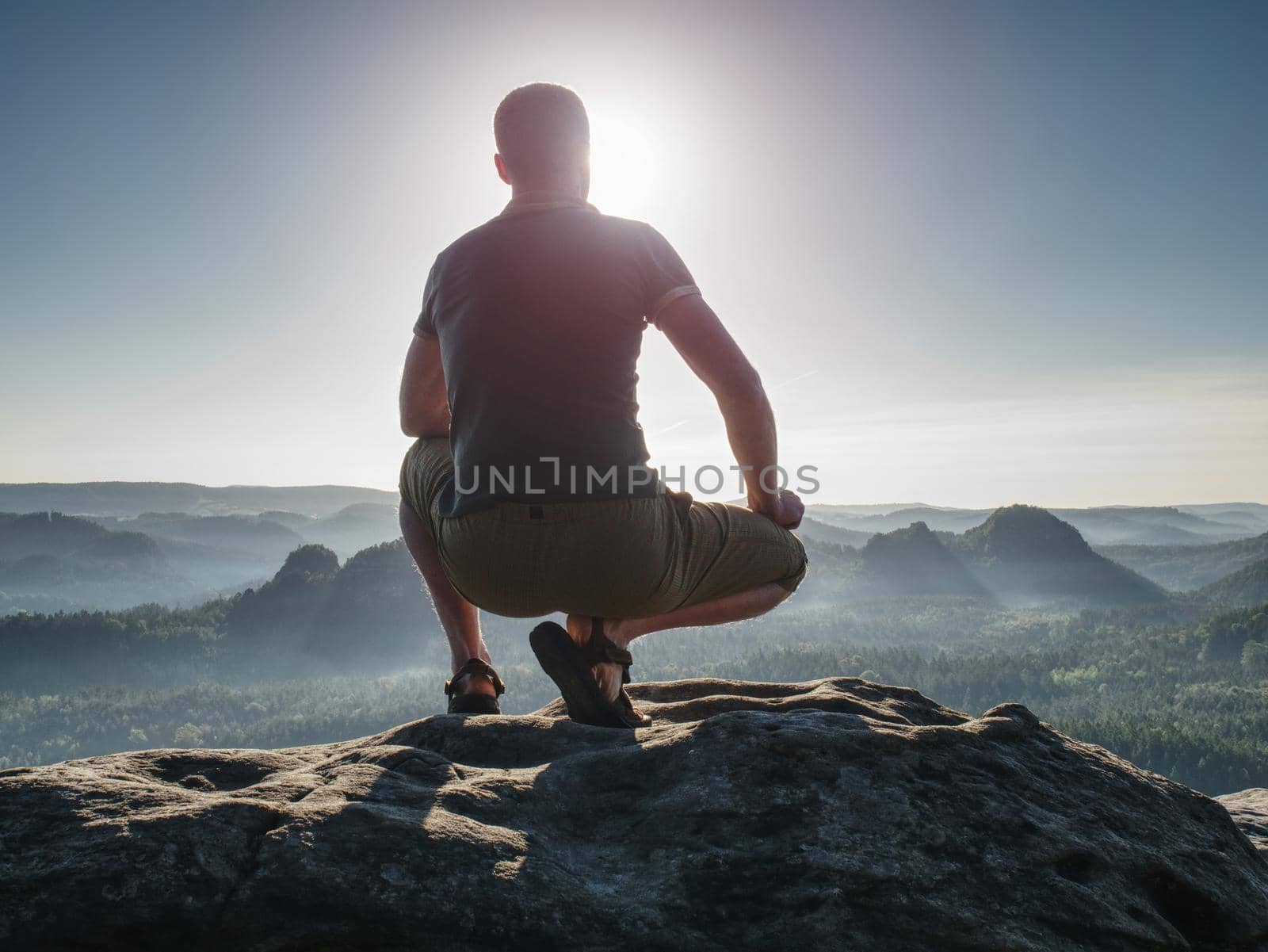 The man standing high on cliff. Hiker climbed up to rocky peak and enjoy view to valley bellow. Foggy mountain peak. Dreamy forrest. Sunrise clouds.