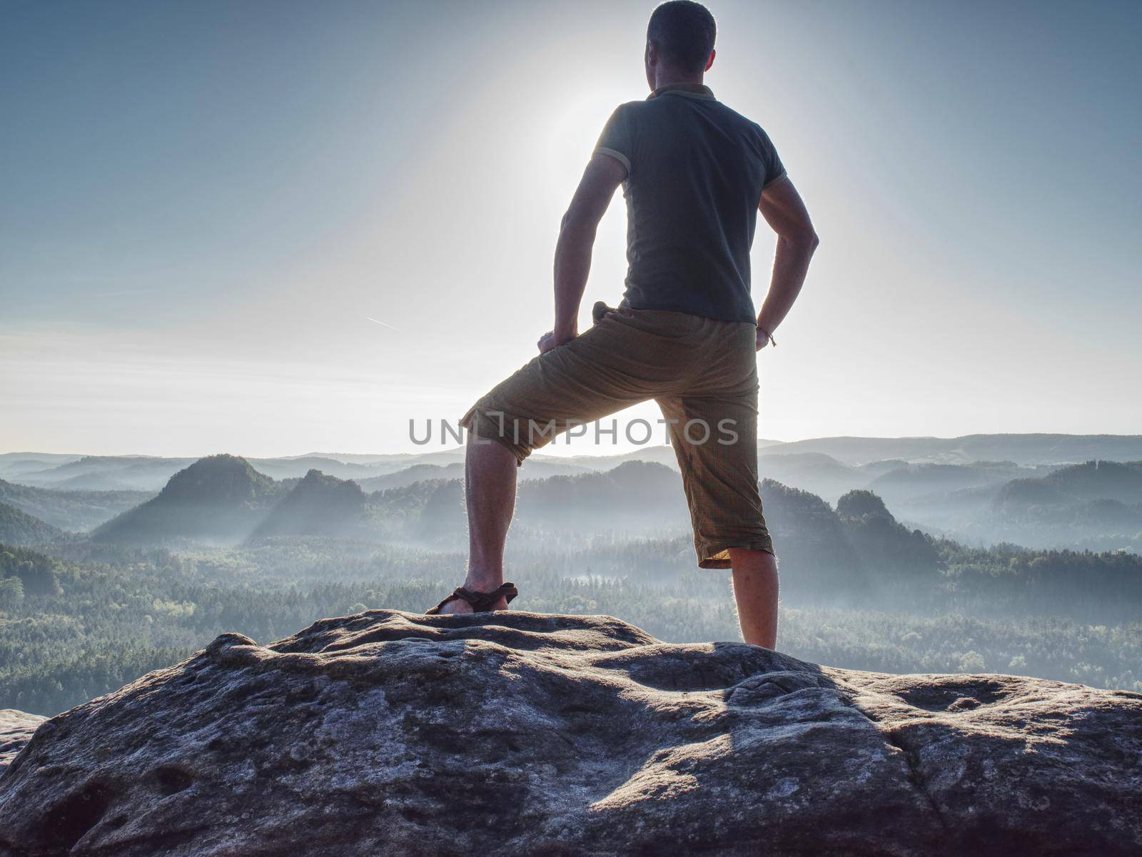 Sports man in outoor clothes and boots walking on rocky peak.  Summit of mountain and look on the nice fog view. Concept freedom