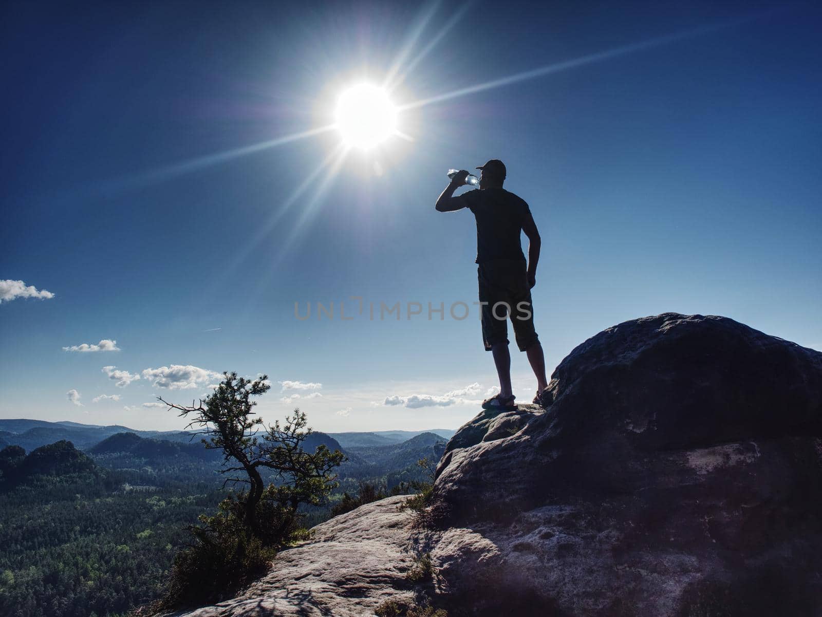 Traveler on rock drinking bottled water from plastic bottle by rdonar2