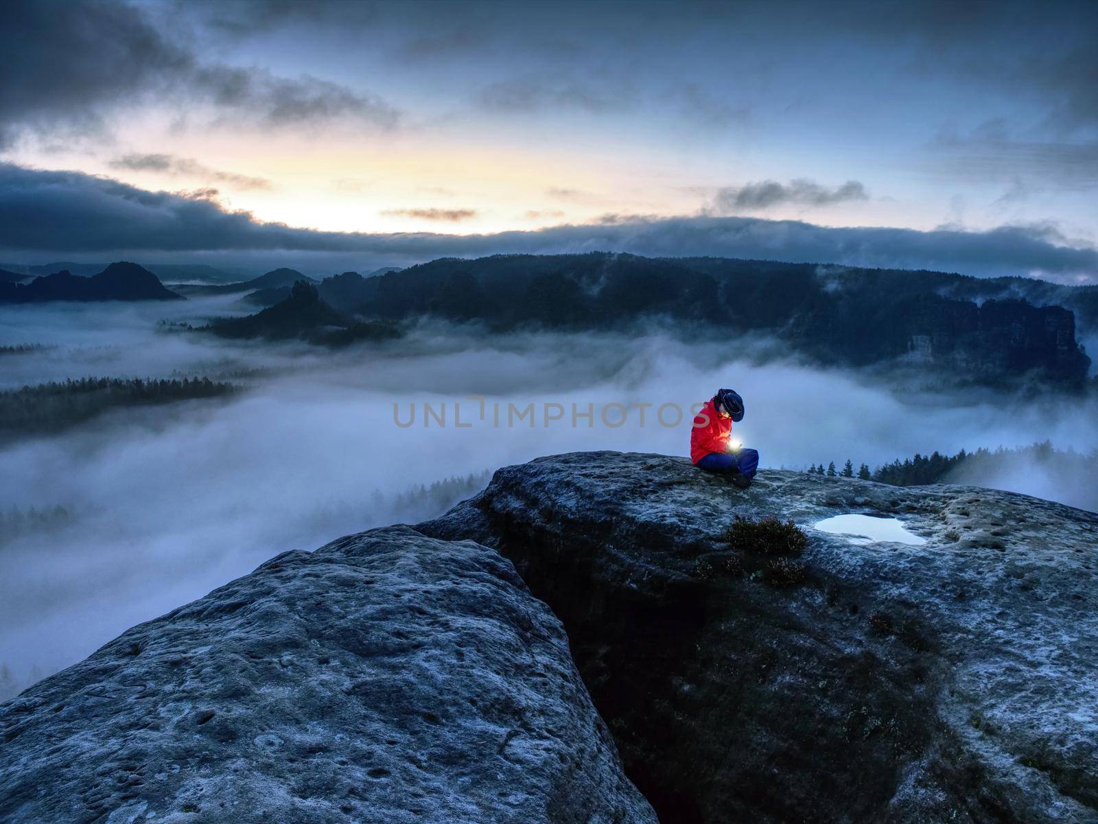 Nice woman sit on summit in hands holding flash bolb. Girl waiting in darkness for sun in high mountains during blue hour.