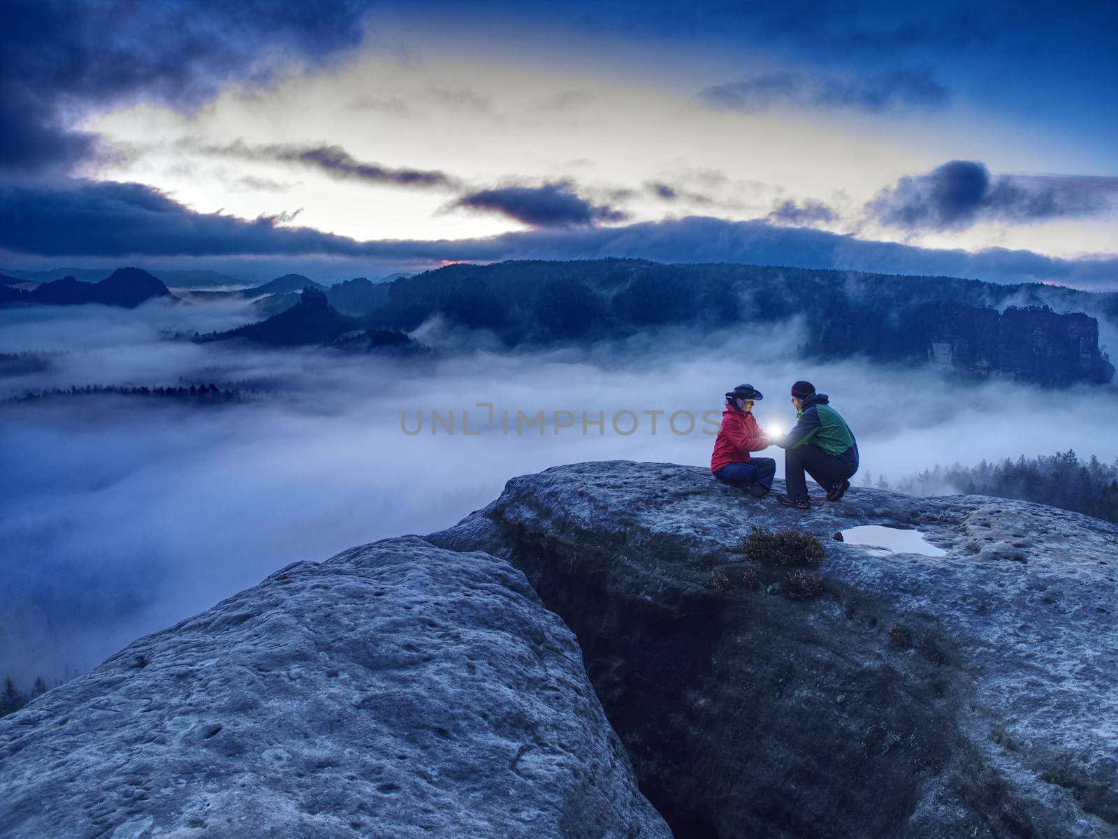 Hikers or climbers in mountains. Couple hold the light  high above danger gulch between rocks. Night photo in misty mountains. Lovers standing on rocky mountain peak