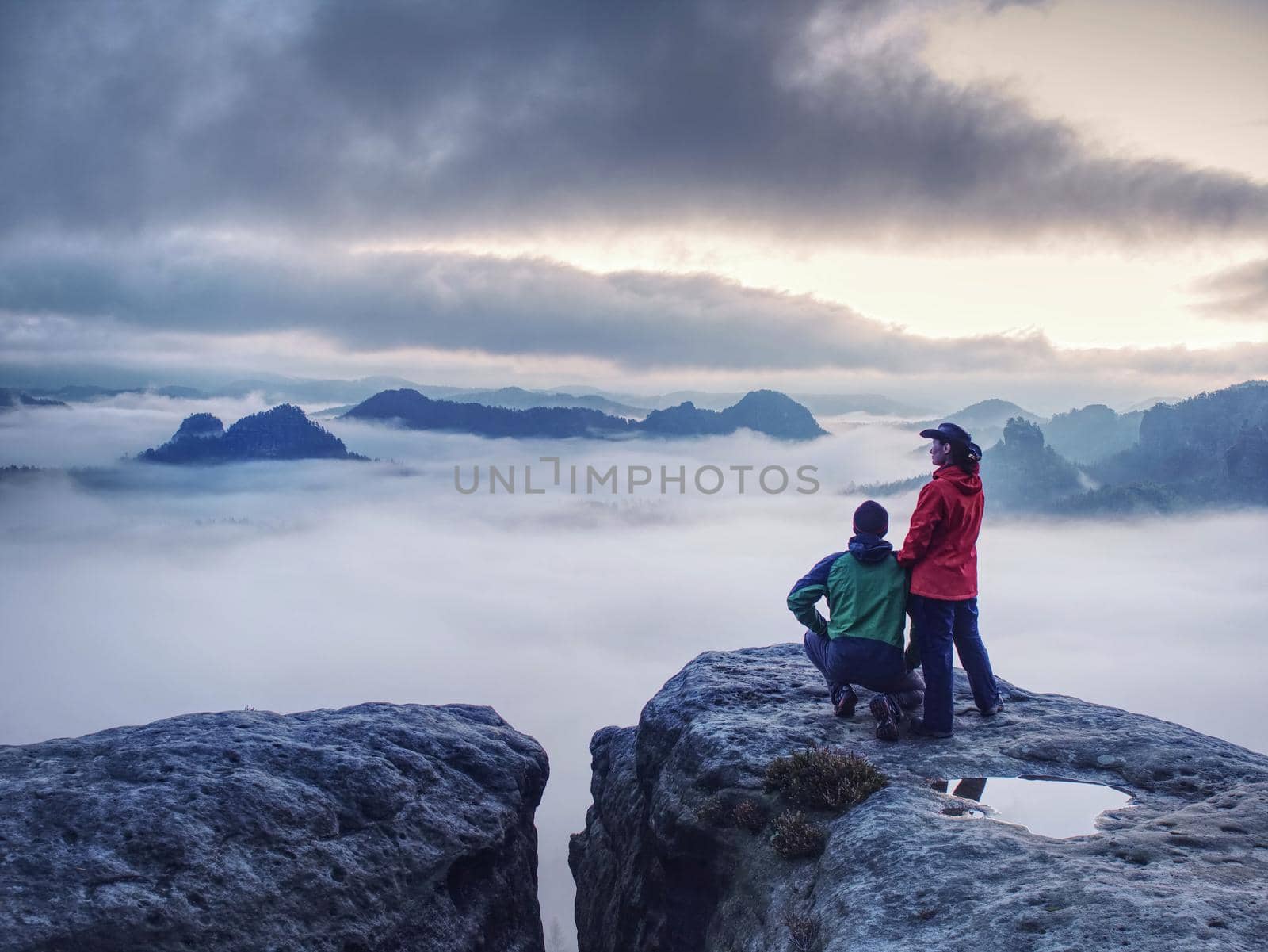 Night photo A woman shows magical lightning lantern to her man.  Woman sits on a rock and shines to misty darkness.  First Sun rays appear in the clouds