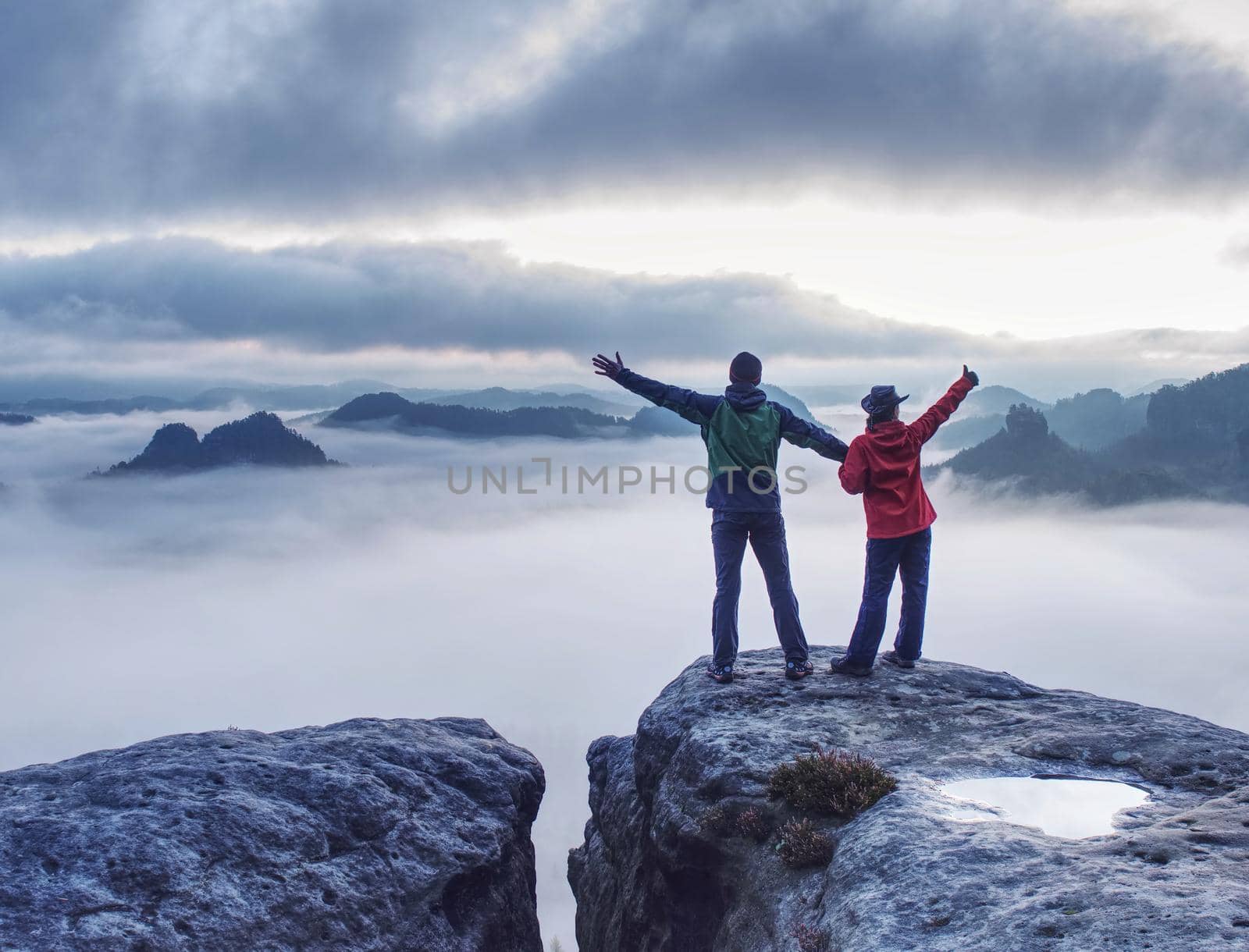 Couple on the mountain looking over heavy mist to  the horizon. Romantic night with the first sun rays in dark clouds in the sky