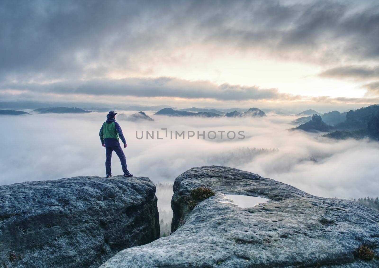 Male hiker finnaly standing on a rock stock and enjoying foggy mountain view 