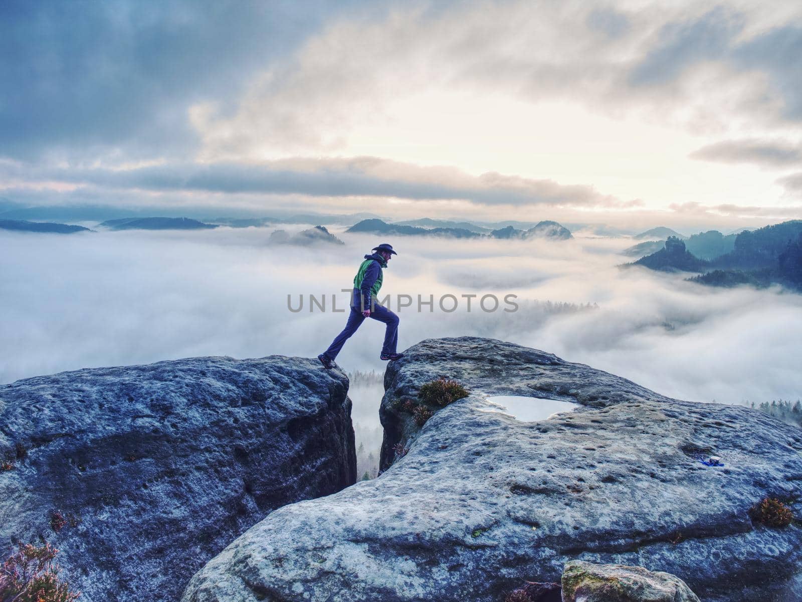 Man on successful hiking trip, silhouette in low mountains of Saxony Switzerland. Hiker on top of mountain looking at beautiful misty landscape