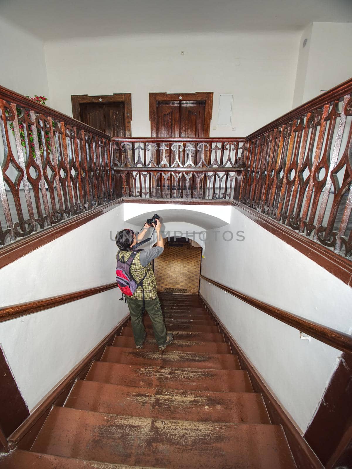 Black hair woman photographer study interier of old house with renewal wooden stairs and wooden handrails around staircase.