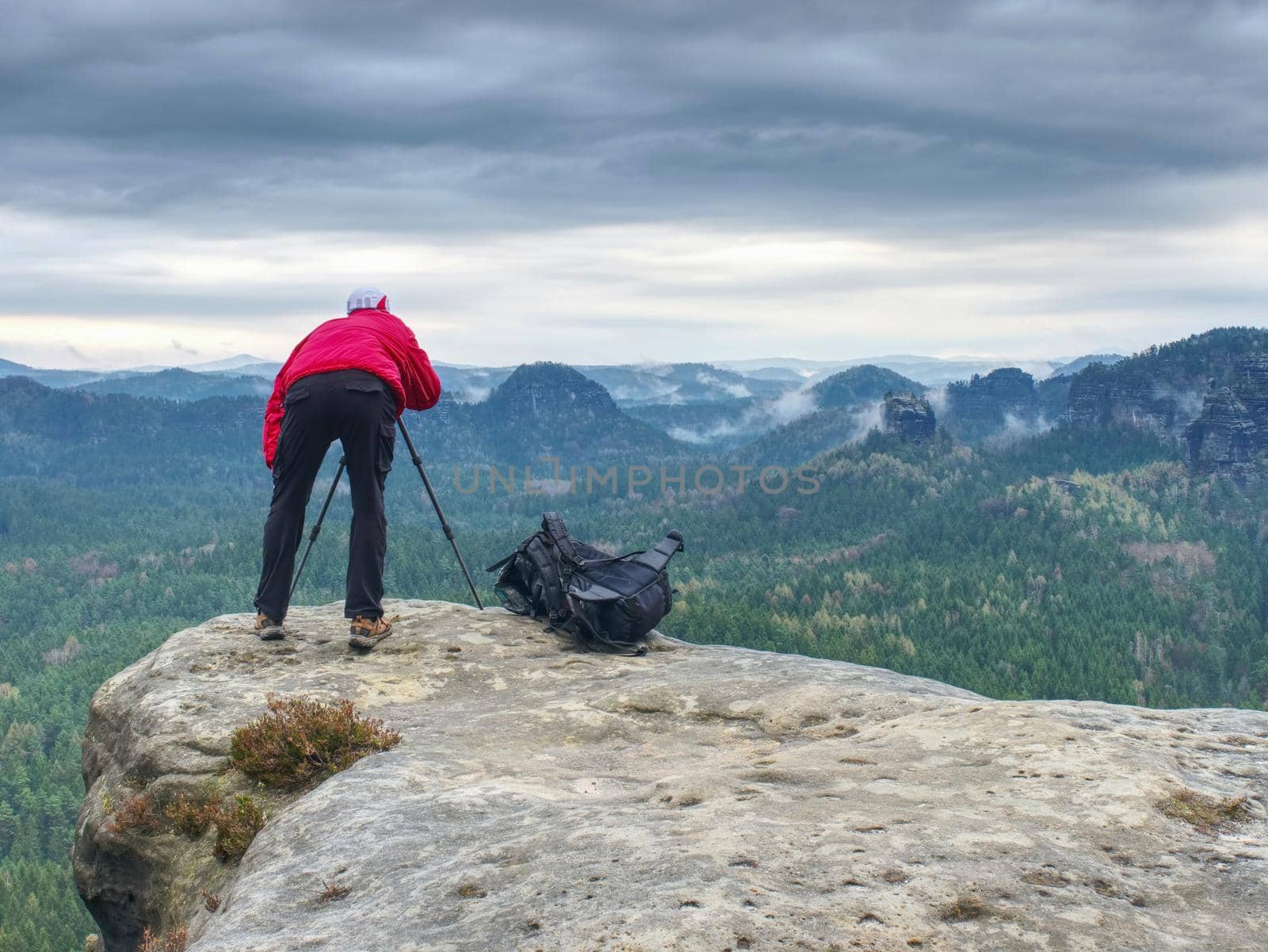 Photographer takes photos with camera on tripod on rocky mountain peak.  by rdonar2