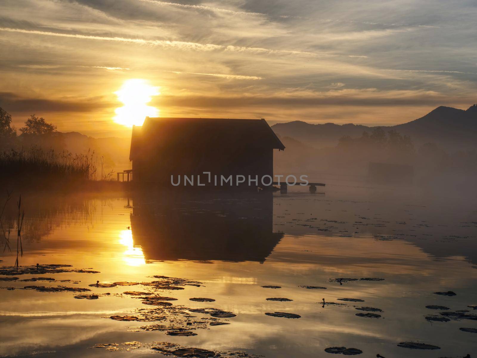Wooden fishing boat shelter built above level of mountain lake. Moody morning view