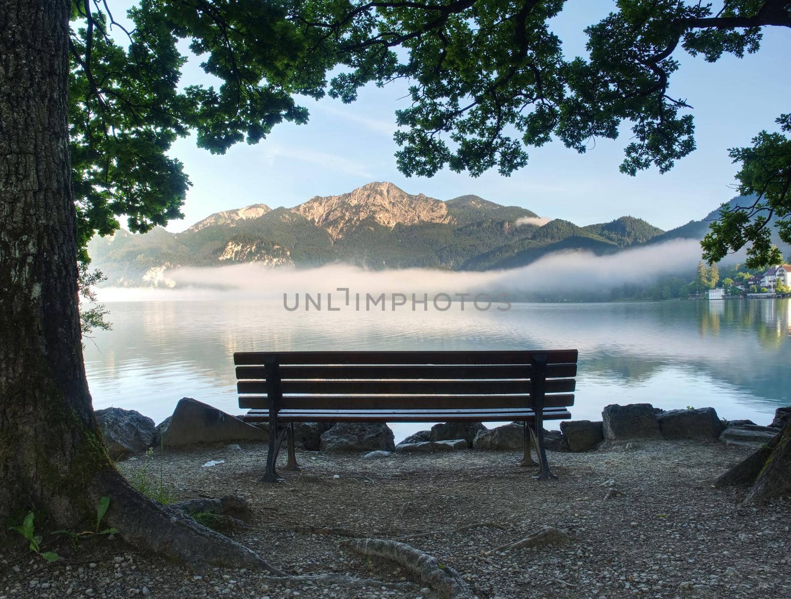 Empty bench at the lake beach. Magnificent lake in South Bavaria, Germany.  The concept of walking and eco-tourism. Water reflects the surrounding mountains and forest