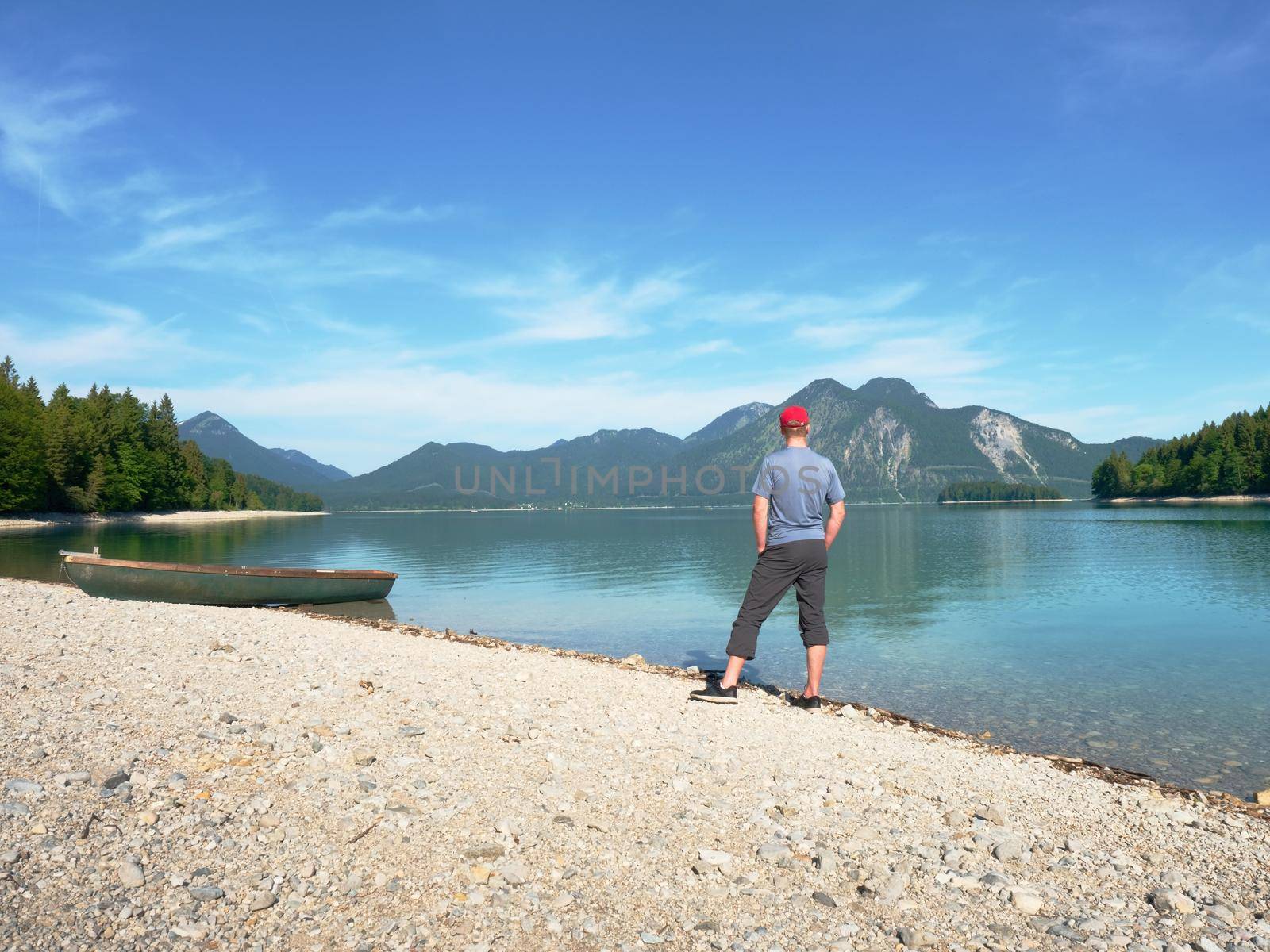 Man stay lonely at the bench in front of the lake. Tourist enjoys beautiful views of mountain lake