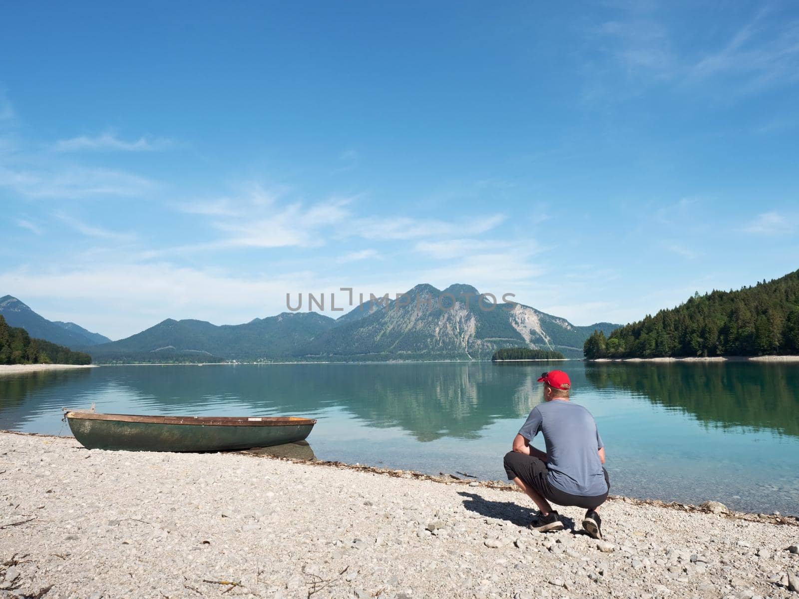 Adult man in blue shirt at old fishing paddle boat at mountains lake by rdonar2