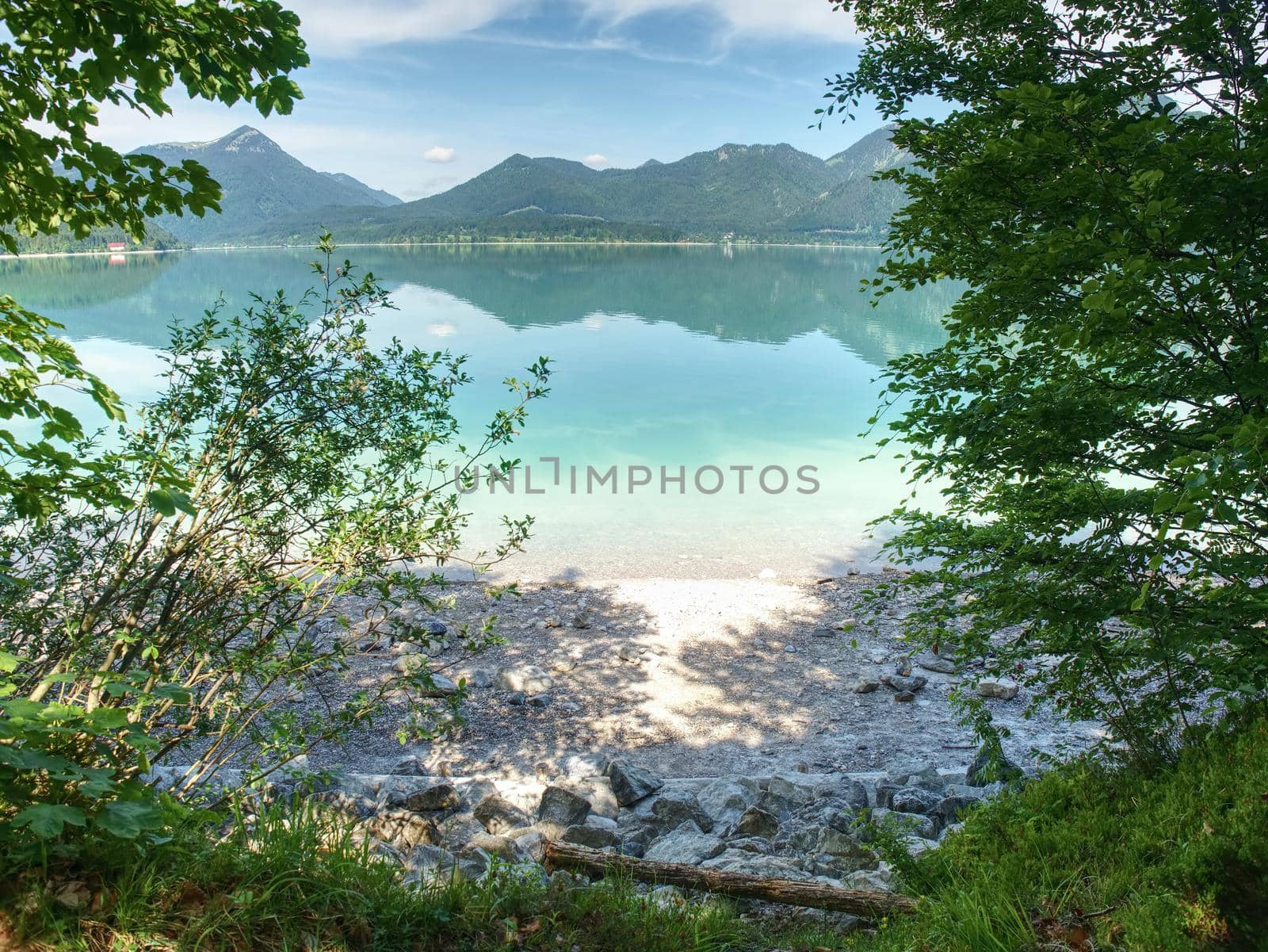 Pebble or rocky shore of the mountain lake, in the distance you can see the sharp Alps mountains