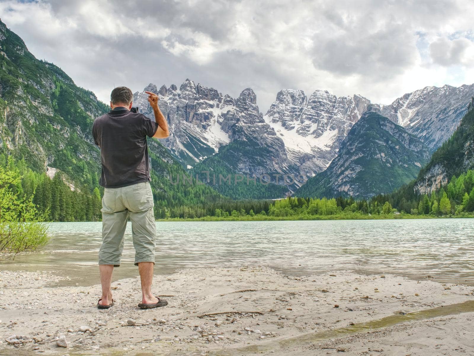 Photographer with eye at viewfinder is taking photo of lake with Alps by rdonar2