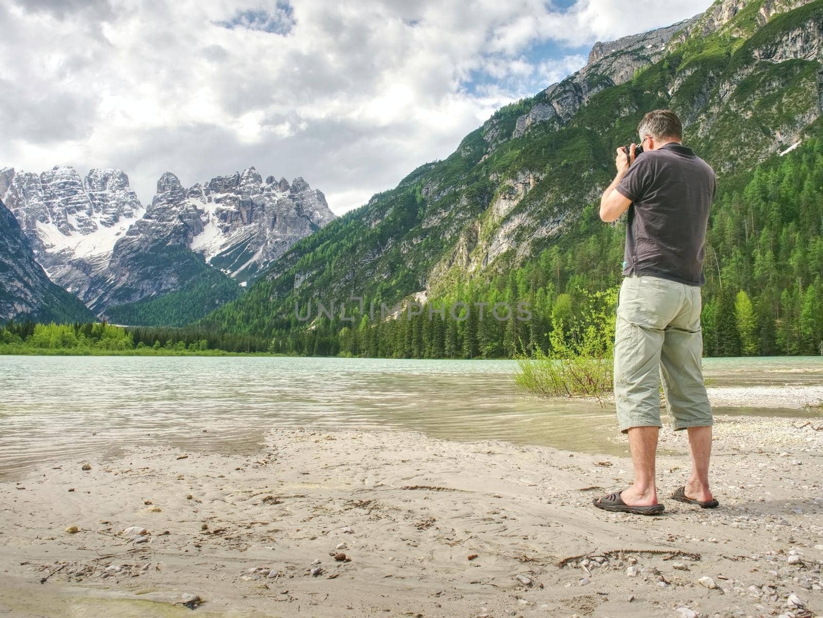 Man hiker is taking photo of ship at mountain lake shore.  by rdonar2