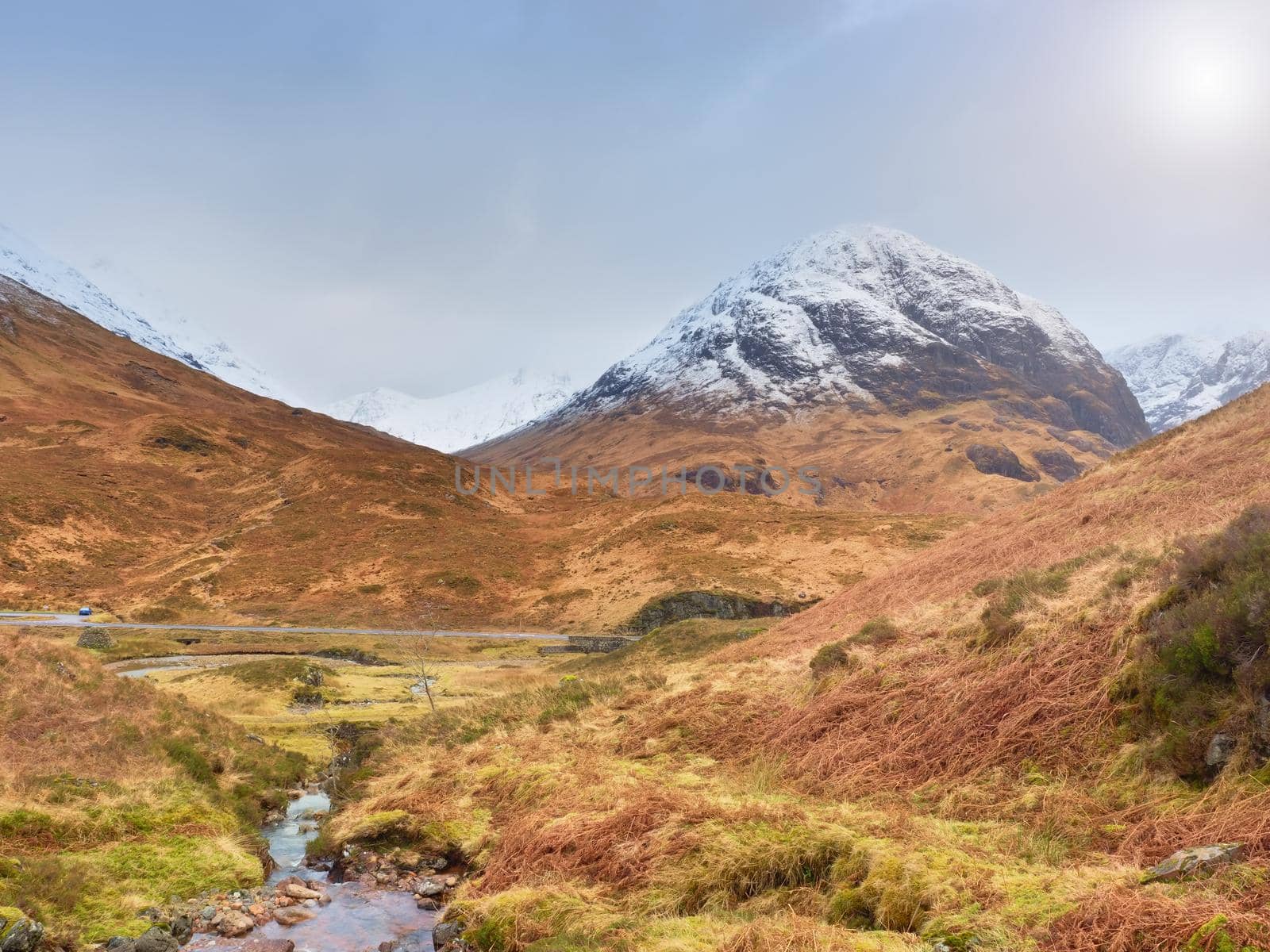 Mountains landscape wild stream in front. White snowy mountain peaks and grey cloudy sky