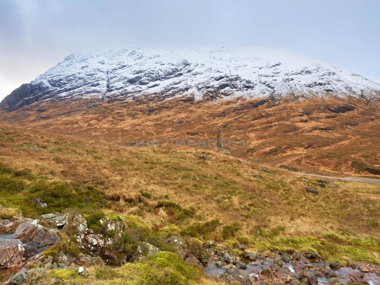 Mountain stream with snow covered peaks in background. Dark sky with low clouds.  by rdonar2