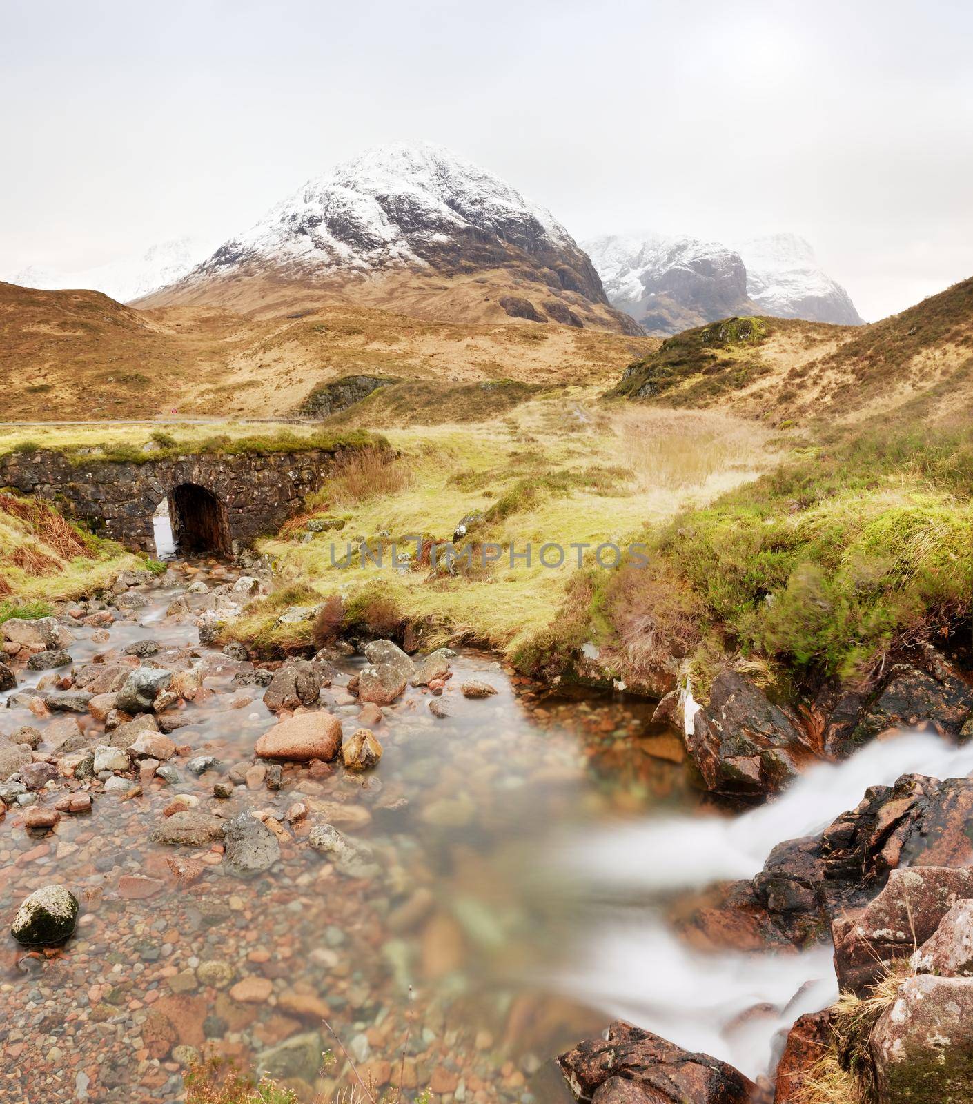 Stream and stony bridge  in spring Higland mountains in Scotland. Snowy mountains in heavy clouds.  by rdonar2