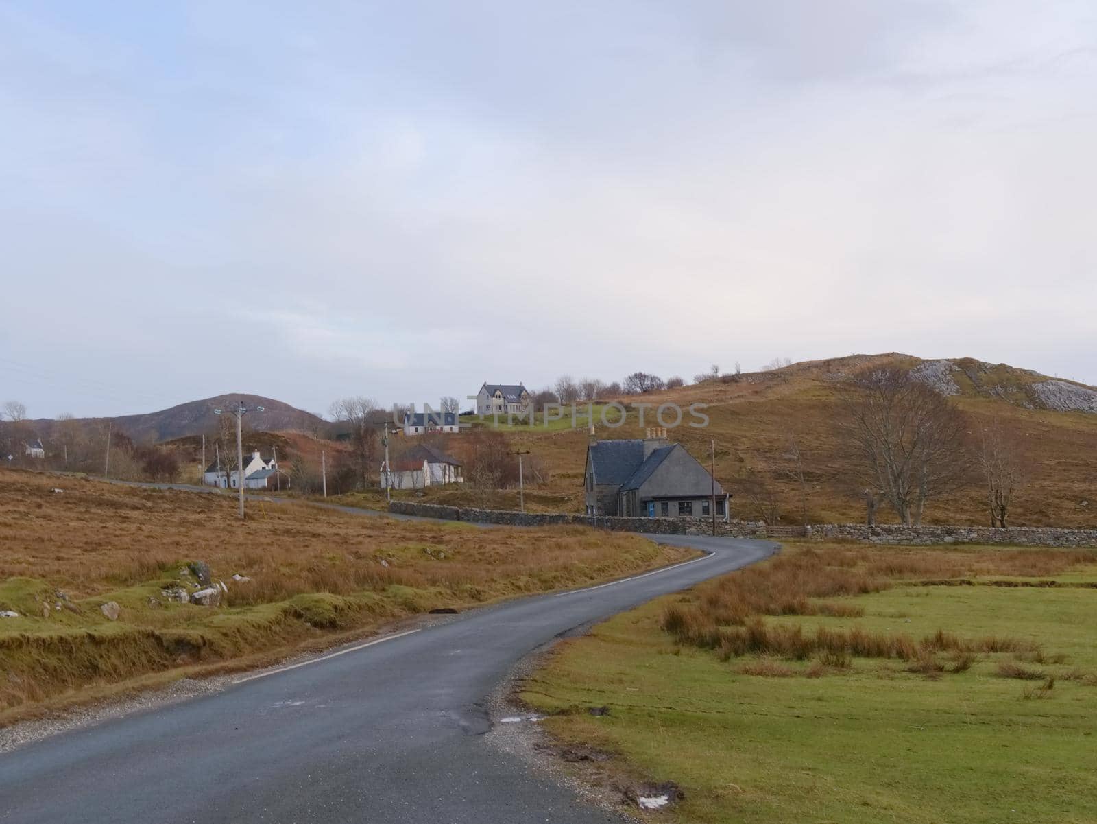 View over  autumnal orange bare landscape, sinle road,  meanders, high  rocky hills and past pastures.