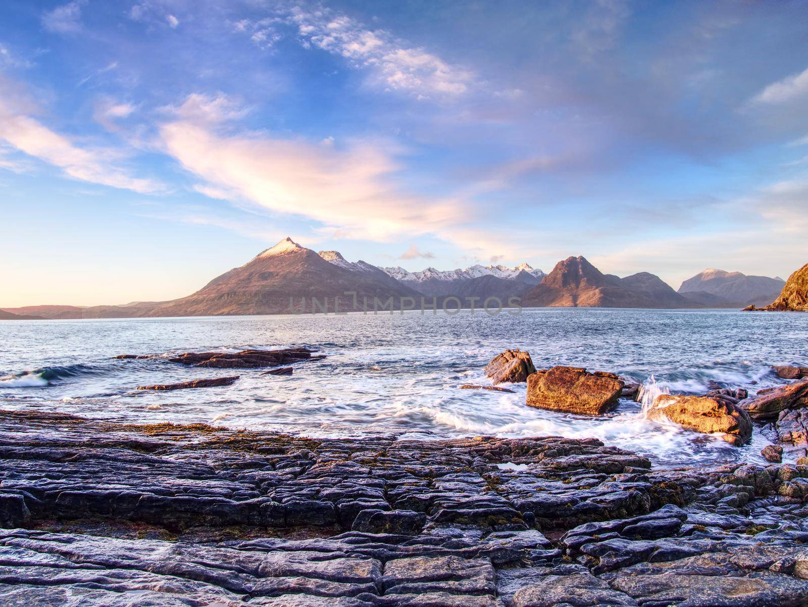 Peaceful dawn at Elgol bay. Low angle  overlooking of offshore rocks and smooth sea, mountains at horizon. Winter  Isle of Skye, Scotland 