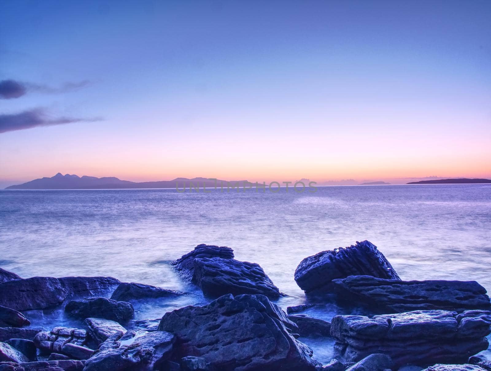 The stony beach and cliff of rocky bay. Blue tones of February sunset, pink horizon.  by rdonar2