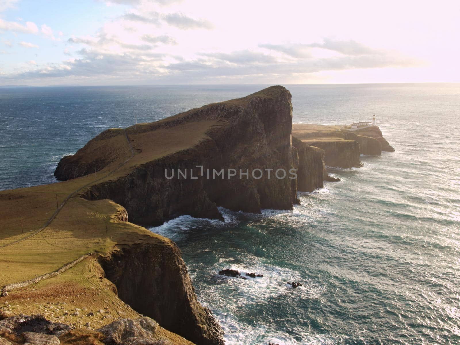 The Neist Point lighthouse on the end of  world. Foamy blue sea strikes against the sharp cliff.  The Isle of Skye, Scotland