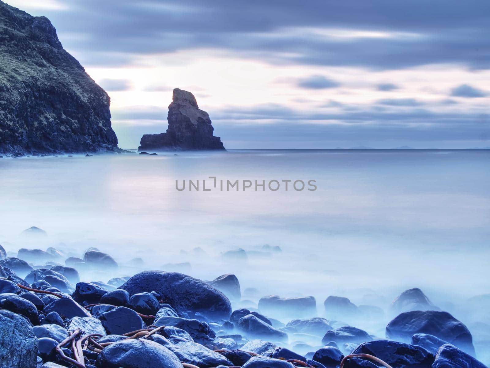 Tranquil stony bay in Scotland after sunset.  Slow shutter speed for smooth water level and dreamy effect