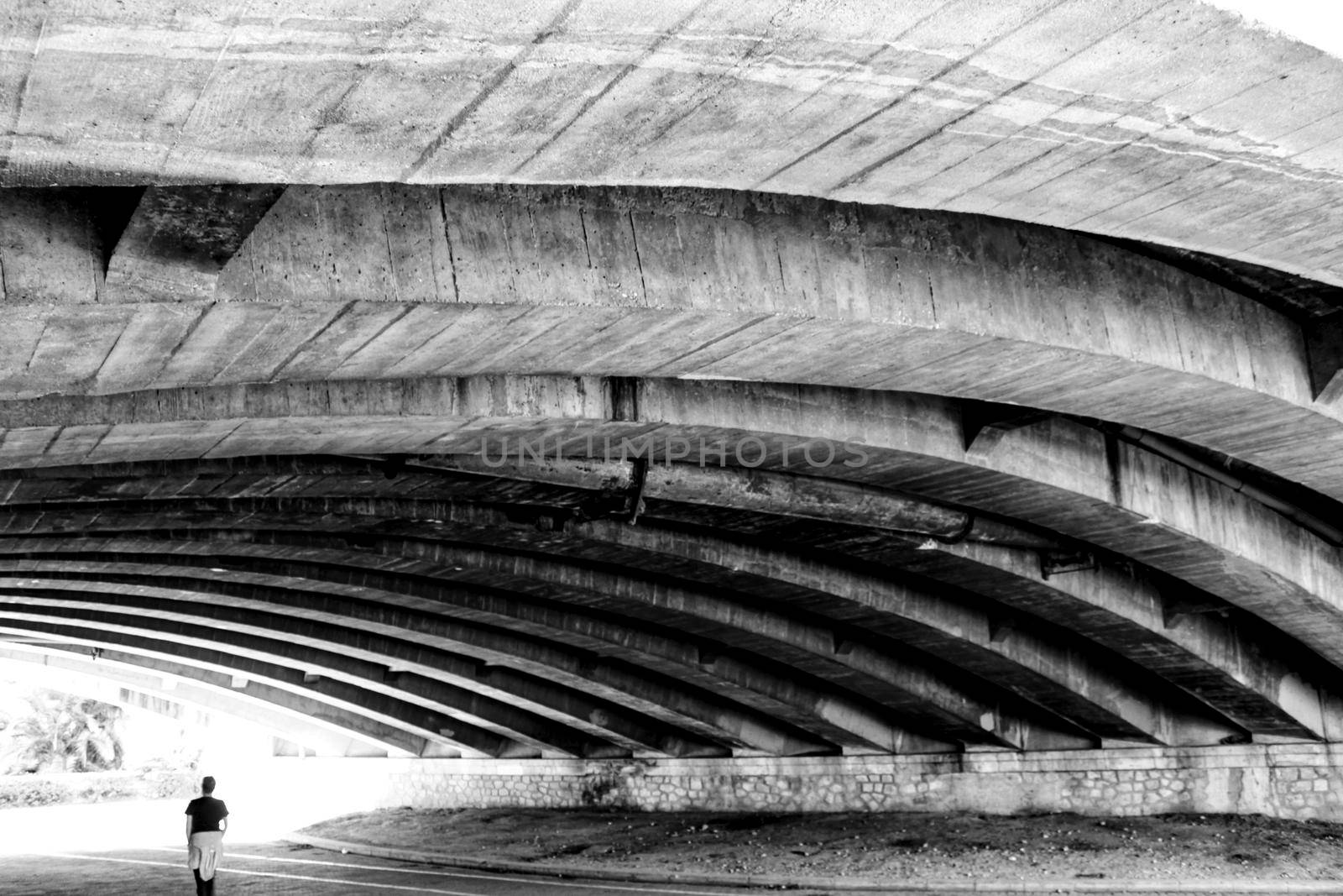 Person walking under Cement structure of a bridge in Valencia, Spain. Monochrome picture