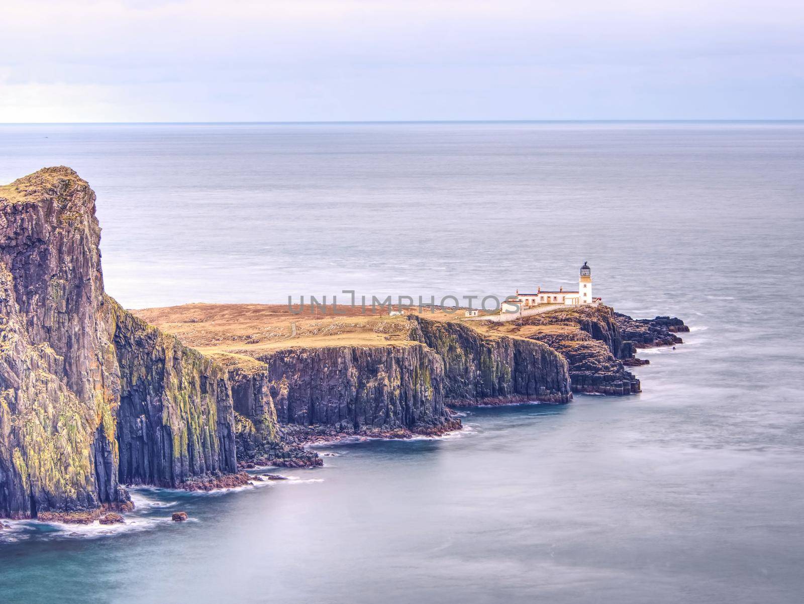 Neist Point peninsula with lighthouse, tourist destination on Isle of Skye, Scotland. Foamy blue sea strikes against the sharp cliff.  All travelers must see