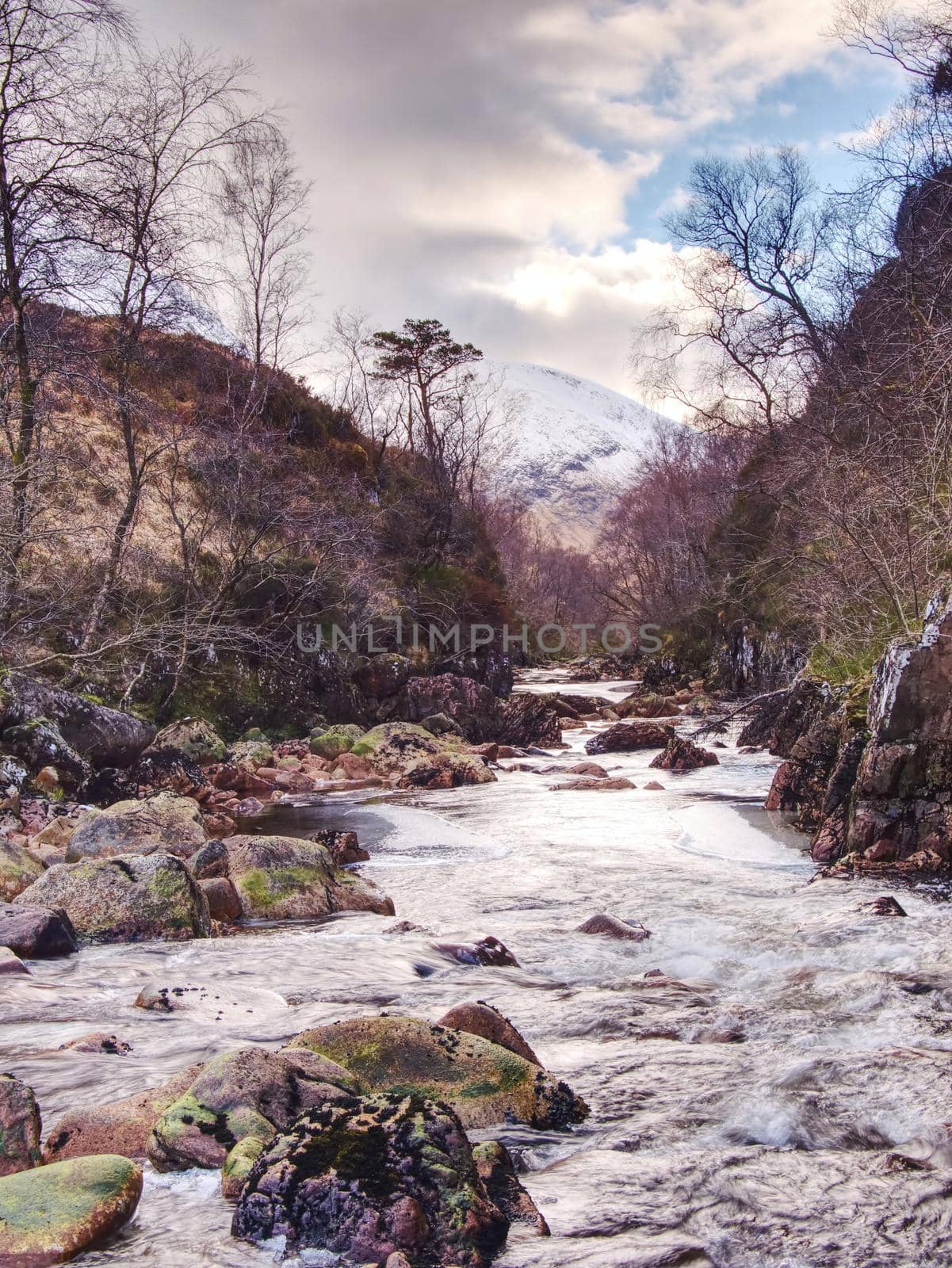 River at base of snowy mountains in Scottish Highlands near Glencoe  in winter. Cold windless winter morning