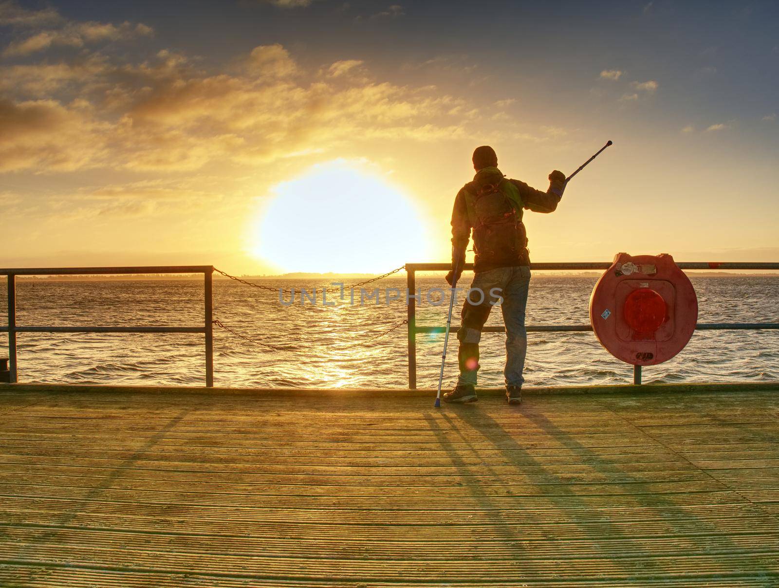 Tourist on ferry boat mole within sunrise or sunset. Warm colors, reflection of Sun in camera lens. 