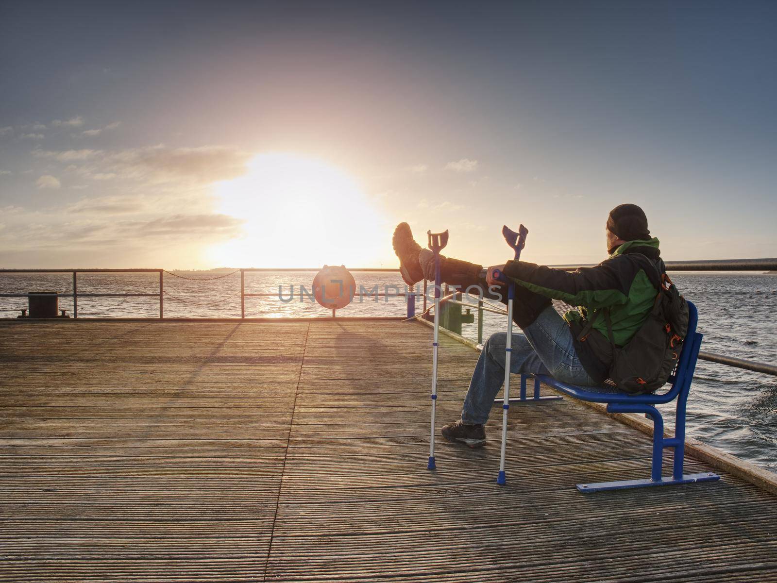 Hurt man having rest, looking into distance and meditating. Person watching sunset sitting against blue sea 