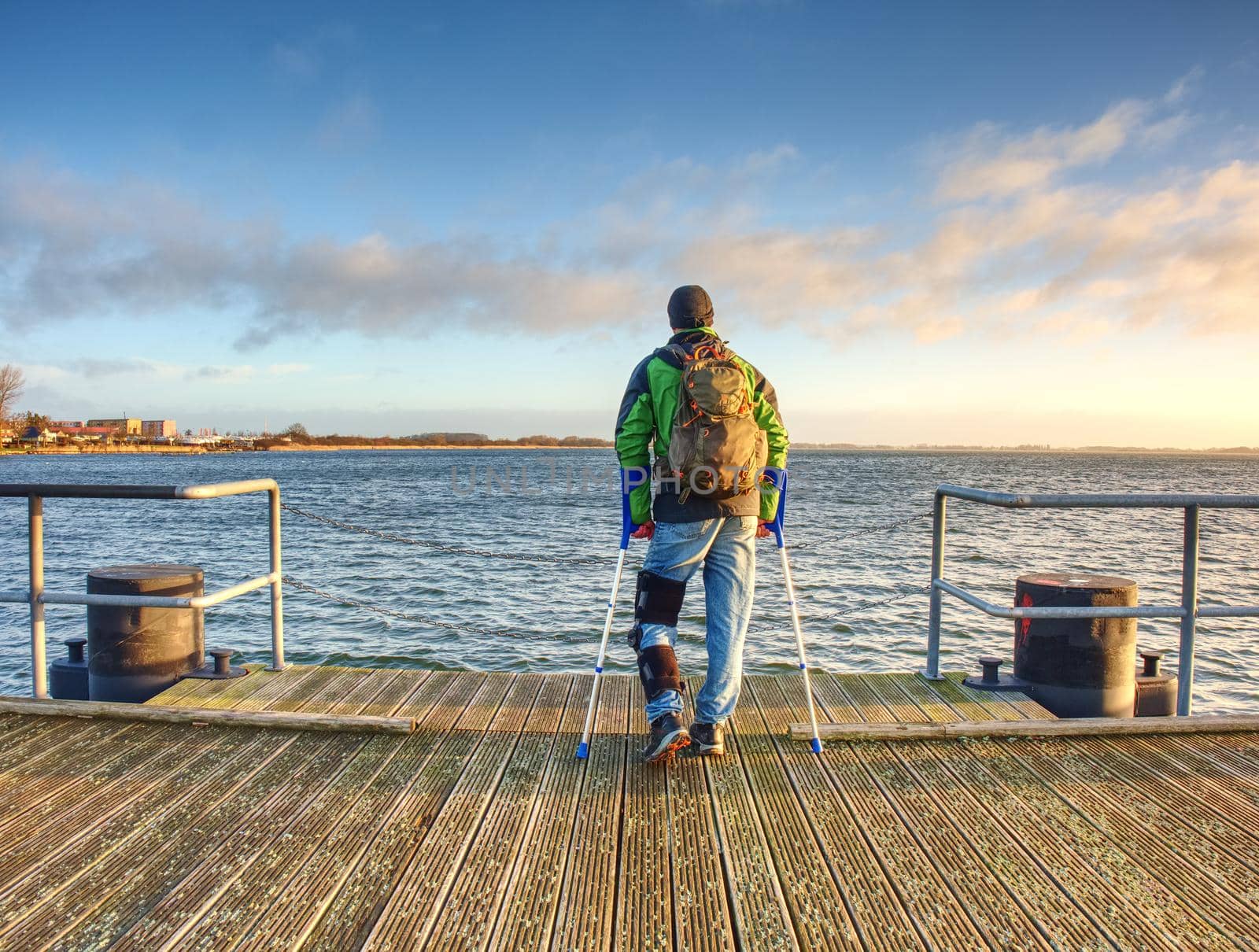 Hurt passenger is waiting for ferry. Empty moring harbor pier, sun above horizon