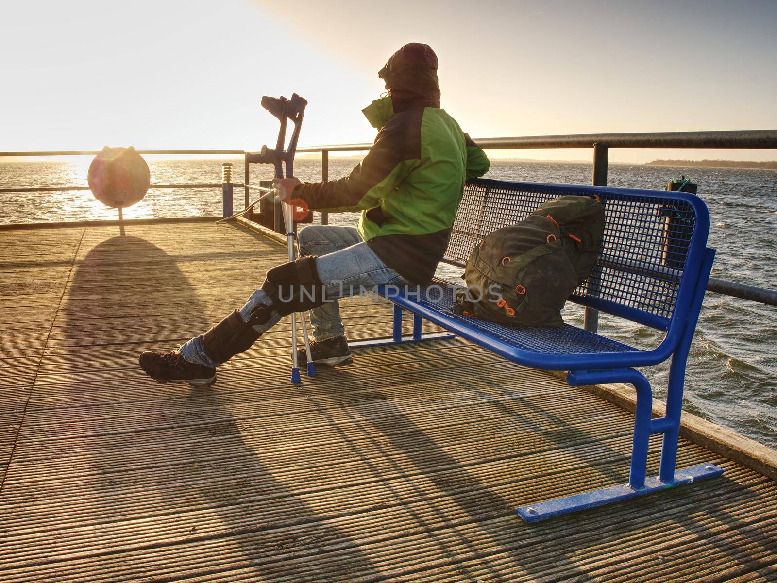 Hurt man having rest, looking into distance and meditating. Person watching sunset sitting against blue sea 