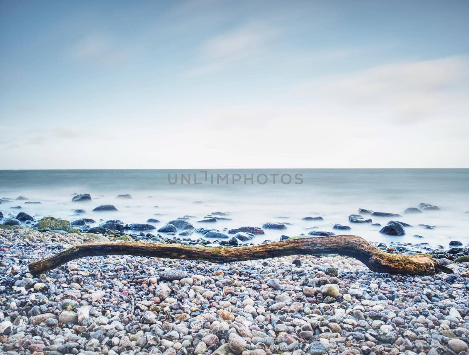 Moody seascape - storm on the sea, turquoise waves breaking on coastal cliffs against cloudy sky. Rocks at water. 