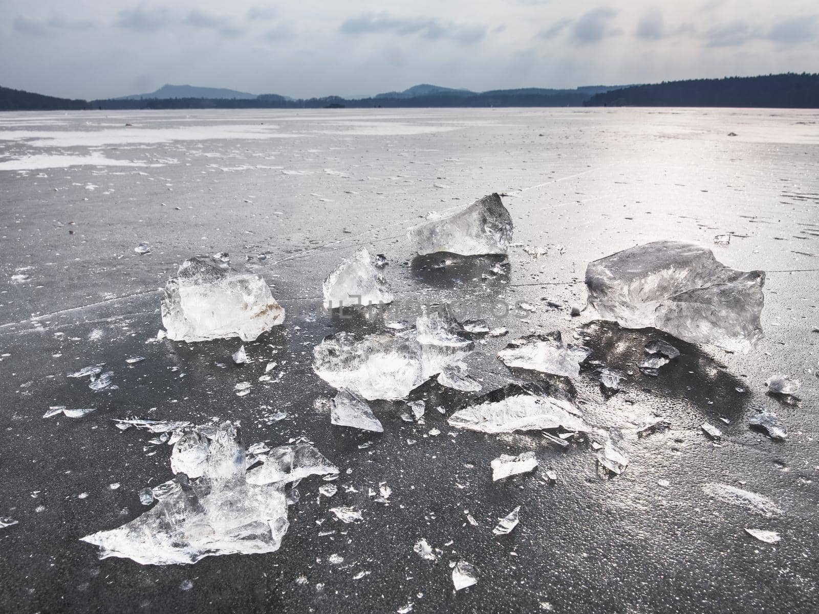 Ice fragments on frozen lake water level. The ice broken into shinning jagged pieces.  Dark natural backlight