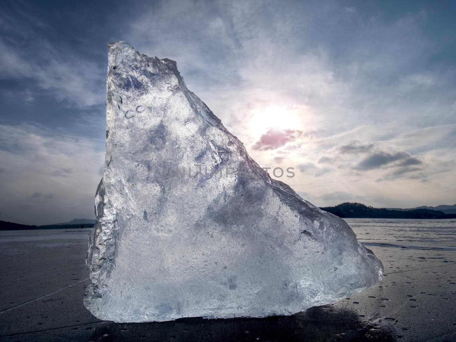 Iceberg piece in the snow floe floating in open ocean. Pink sunset sky in the background. 