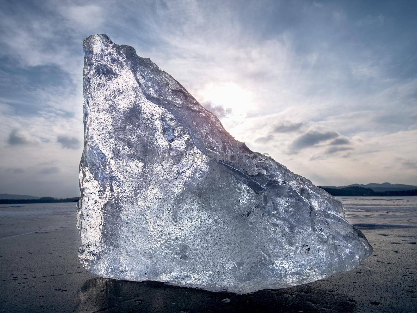 Drifting piece of iceberg and sun glaring on thick ice cover.  Drifting ice floes on  river.