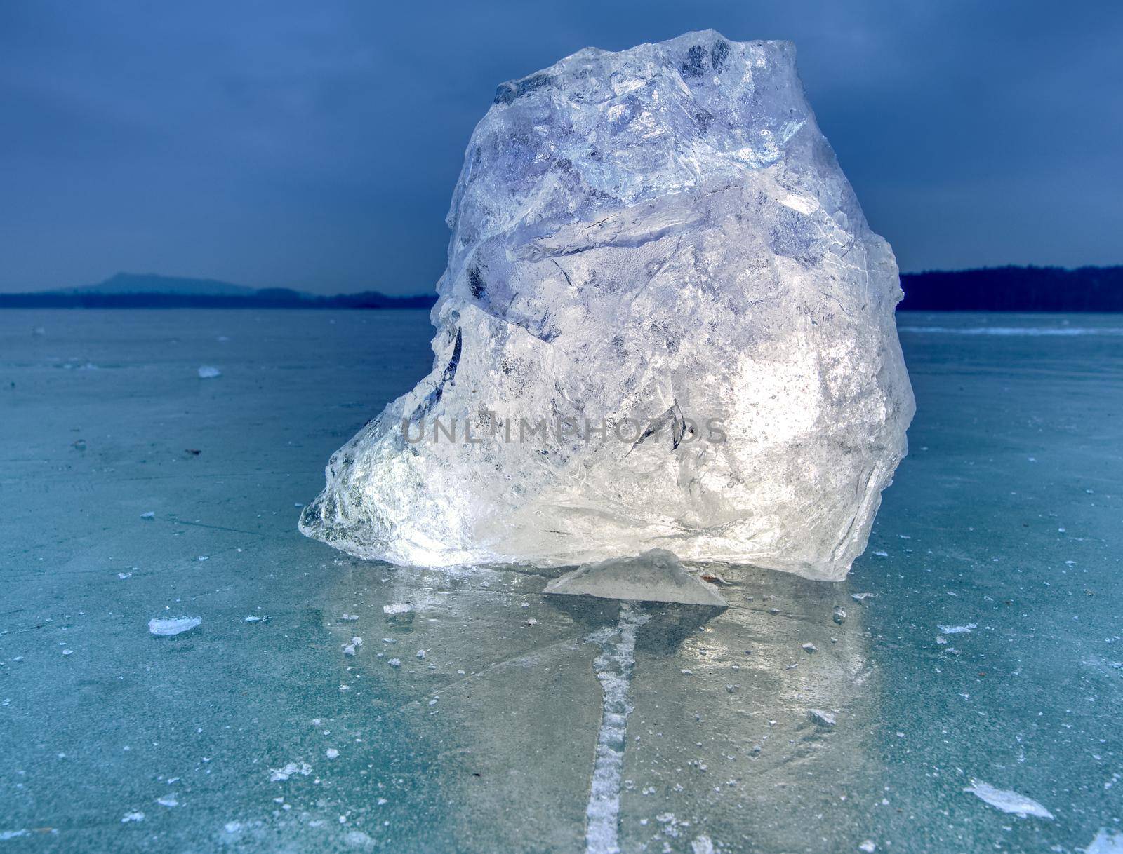 Arctic ice. A large piece of natural ice on a green blue flat ice of frozen lake, water bubbles texture. Shiny detail inside wonderful of transparent. stalactite ice.