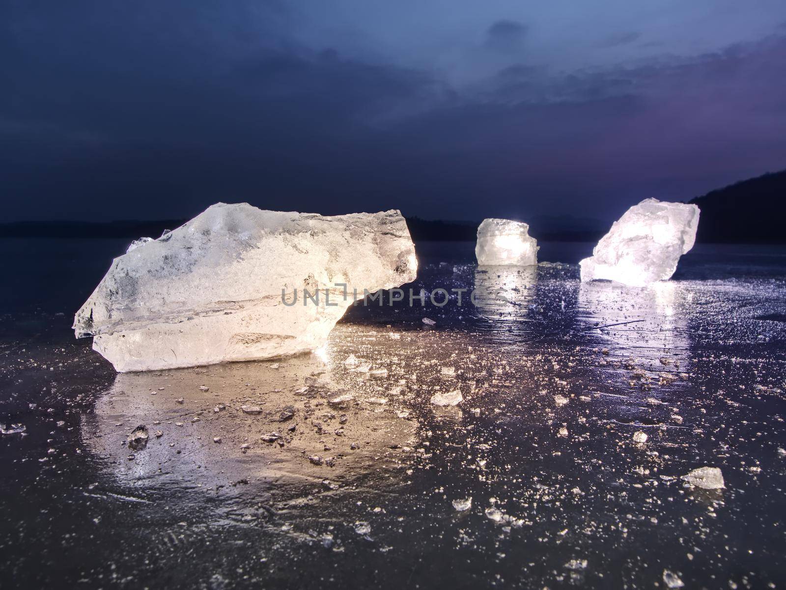 Detail view into  an ice with deep scratches and cracks. Cut floe against to evening sky and spot light.