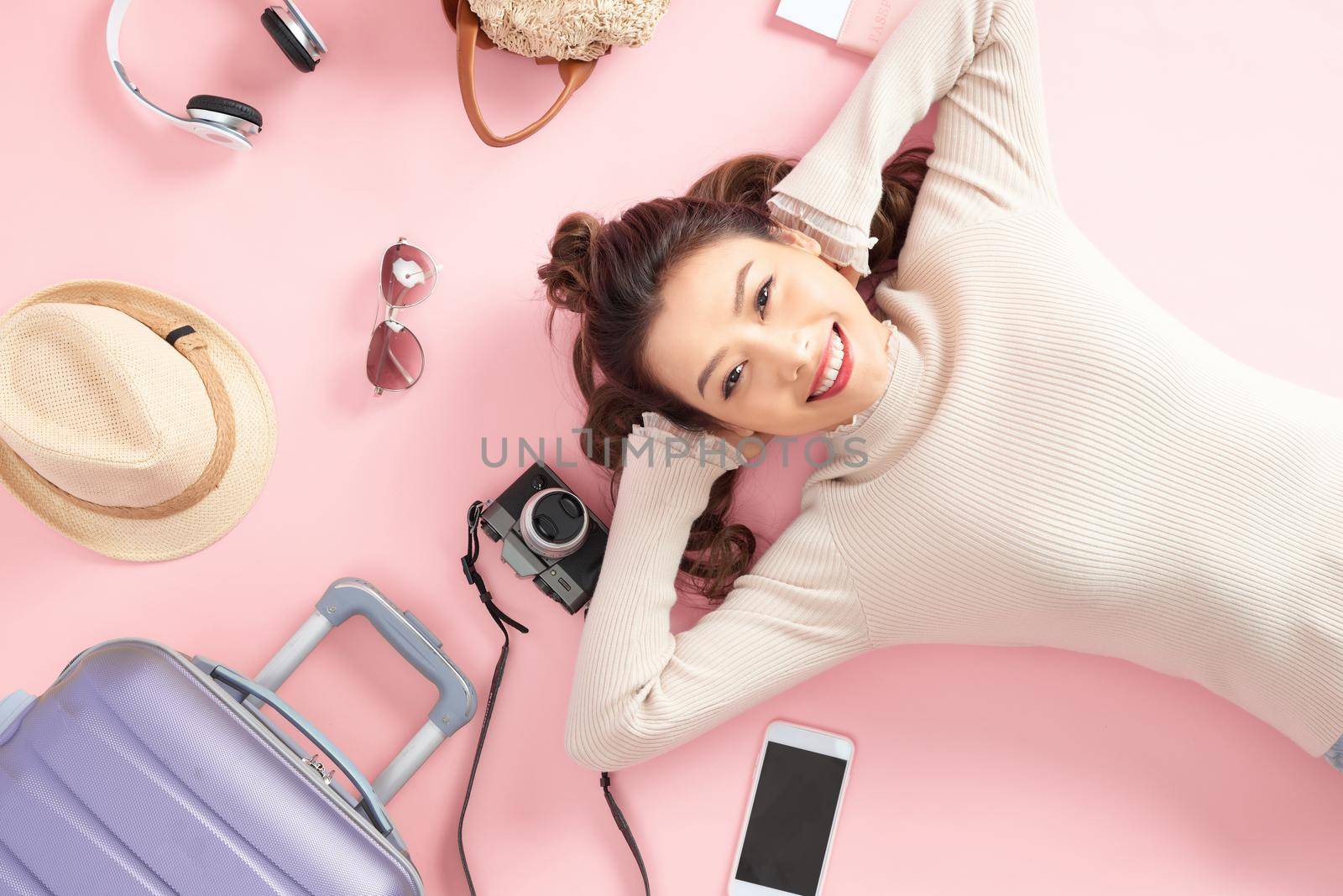 Travel woman smile happily and look somewhere lying on pink floor. Top view