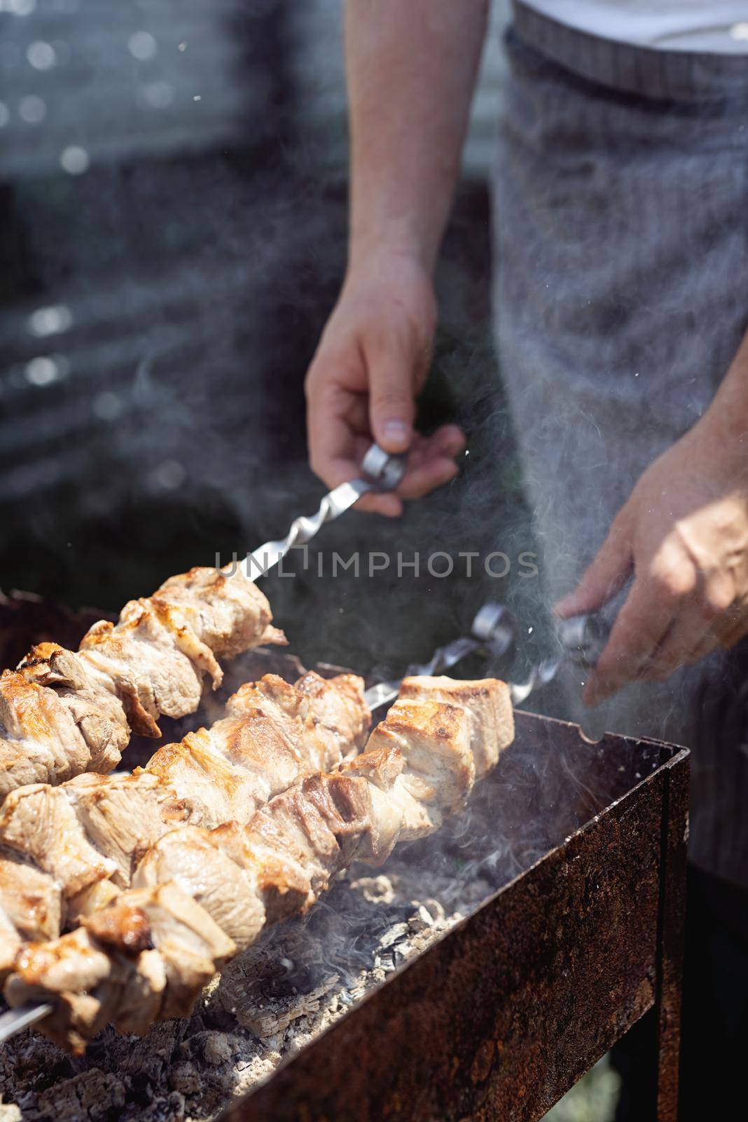 Backyard barbecue. Mans hands grilling kebab on metal skewer fresh meat.