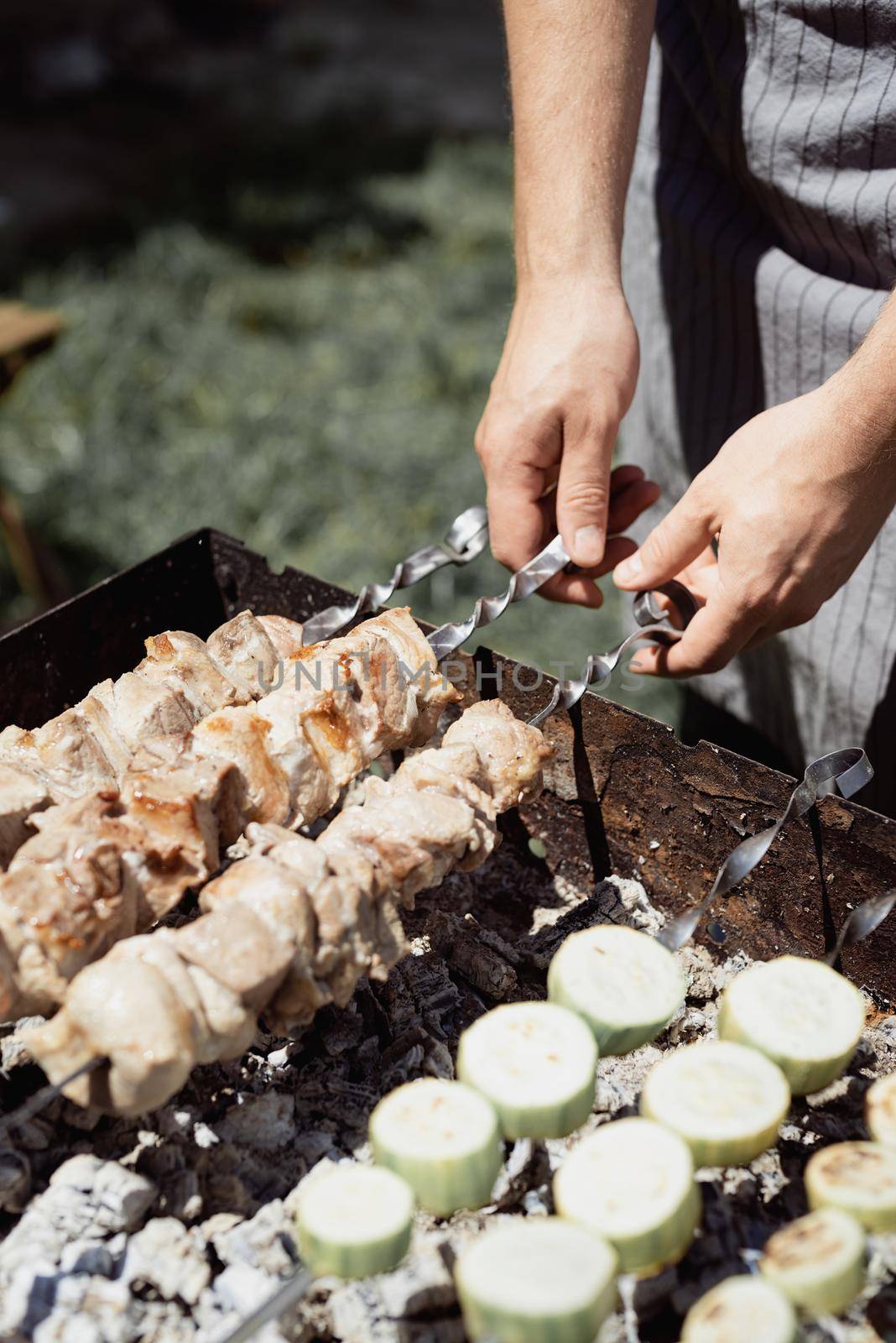 Backyard barbecue. Mans hands grilling kebab and vegetables on metal skewers.