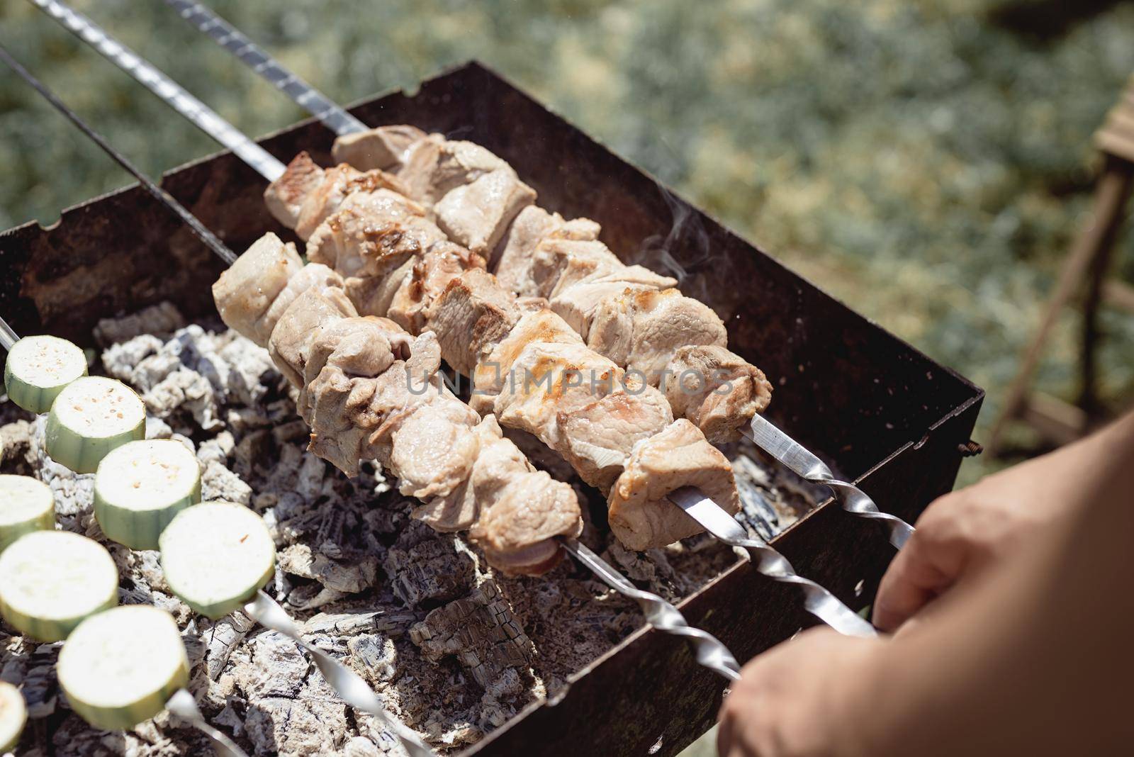 Backyard barbecue. Mans hands grilling kebab and vegetables on metal skewers.