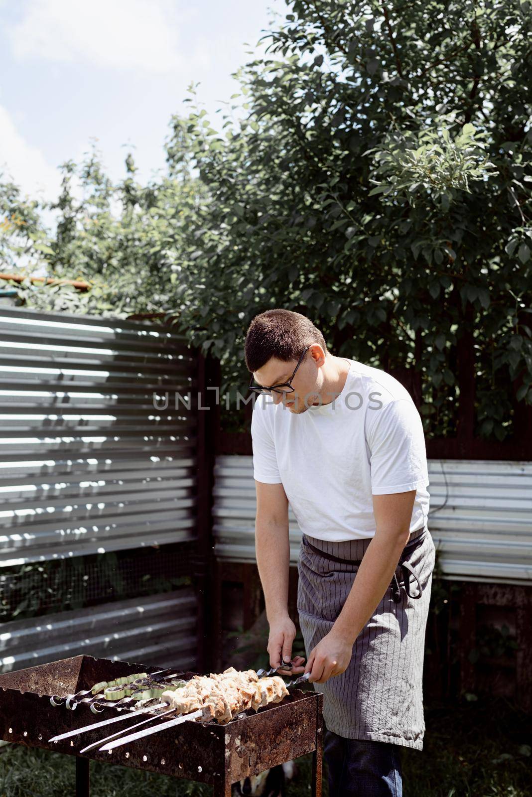 Young man grilling kebabs on skewers, man grilling meat outdoors by Desperada