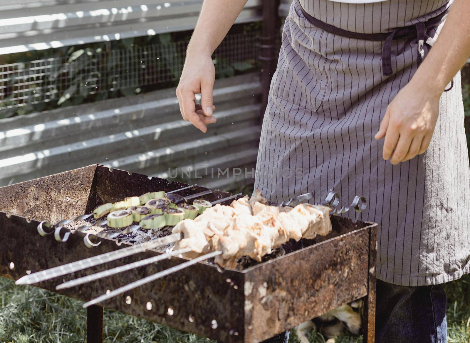 Backyard barbecue. Mans hands grilling kebab and vegetables on metal skewers.