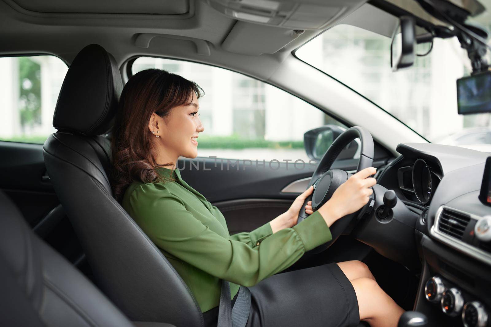 Driving around city. Young attractive woman smiling and looking straight while driving a car