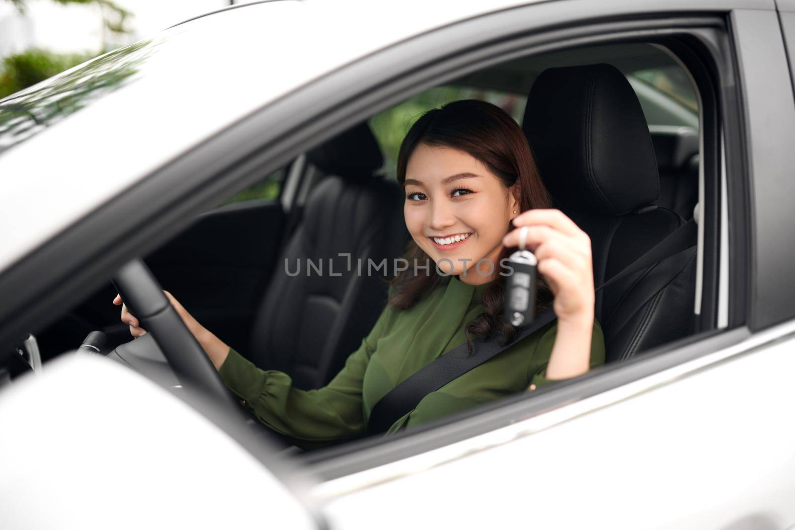 Beautiful young girl driver with car key in hand, happy owner of a new automobile